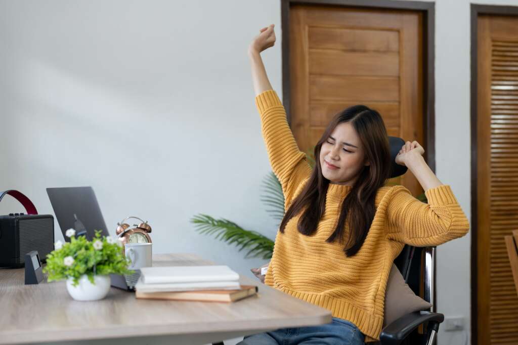 Happy businesswoman warming up body and muscles at workplace, feeling satisfied with work done