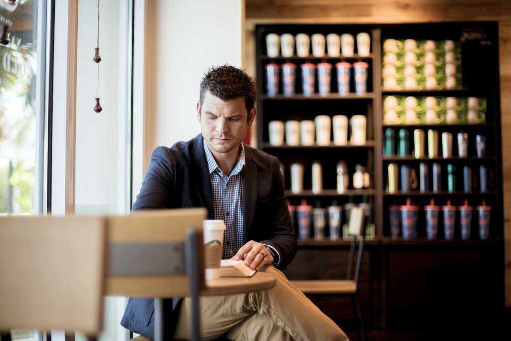 Selective focus shot of a well-dresed male sitting in a cafe while reading the bible
